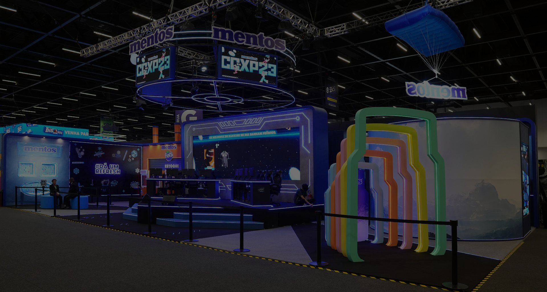 Stand montado e iluminado dentro de um pavilhão de feira, visto do corredor